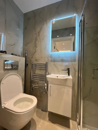 Luxurious marble-tiled bathroom with LED mirror, sleek vanity, and glass shower.