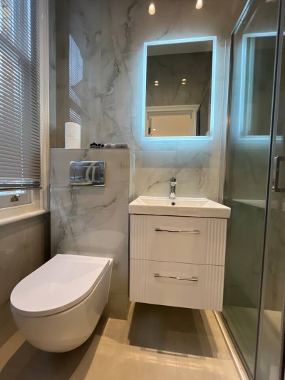 Sleek marble bathroom with vanity, LED mirror, and glass shower for modern comfort.