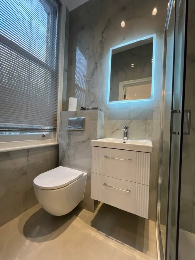 Modern marble bathroom with LED mirror, vanity, and sleek glass shower enclosure.