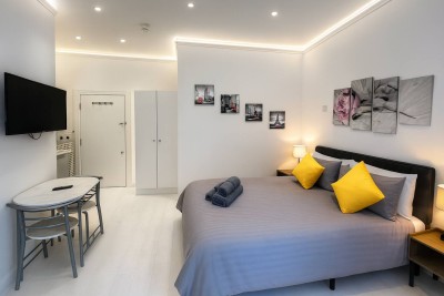 Modern bedroom with grey bedding, yellow accents, wall art, and cozy lighting.