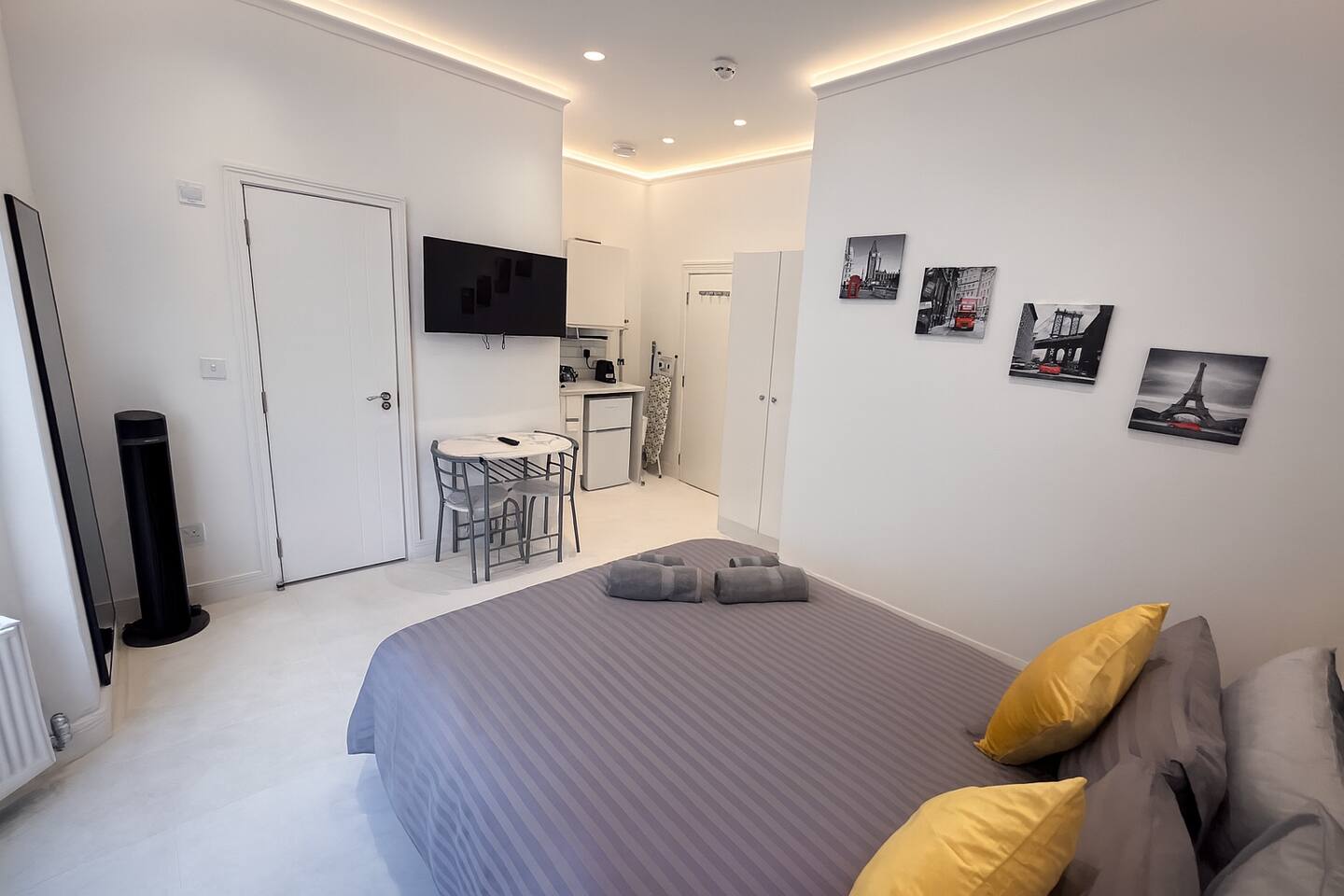 Stylish studio with grey bedding, Paris wall art, kitchenette, and cozy dining area.