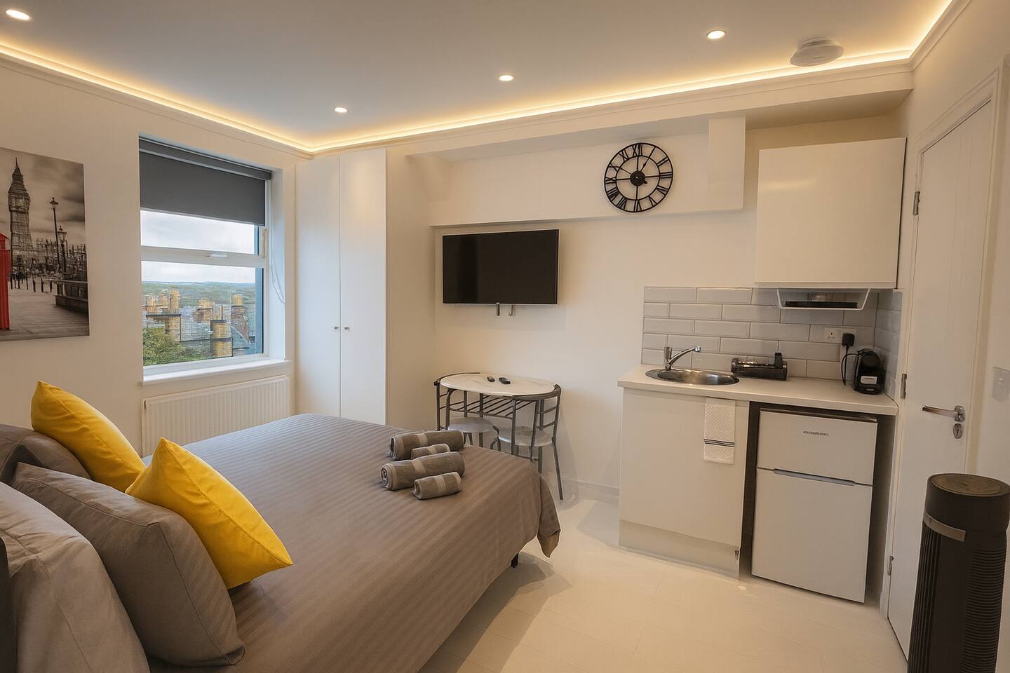 Cozy studio with grey bedding, kitchenette, TV, and scenic window view.