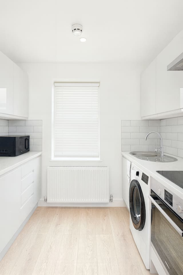 Bright compact kitchen with oven, sink, washer, and sleek modern white cabinetry.