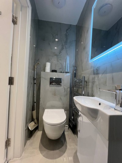 Modern marble bathroom with LED mirror, sleek vanity, and wall-mounted toilet.