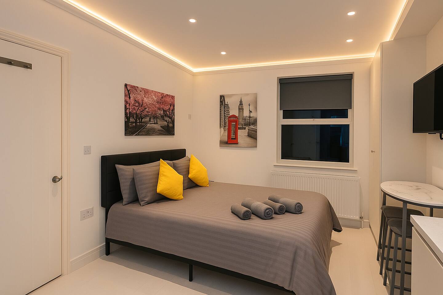 Cozy bedroom with grey bedding, yellow accents, London art, and warm ambient lighting.