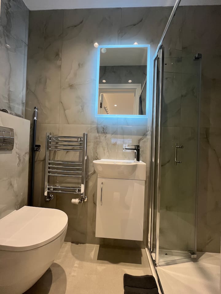 Modern marble bathroom with LED mirror, vanity, and sleek glass shower design.