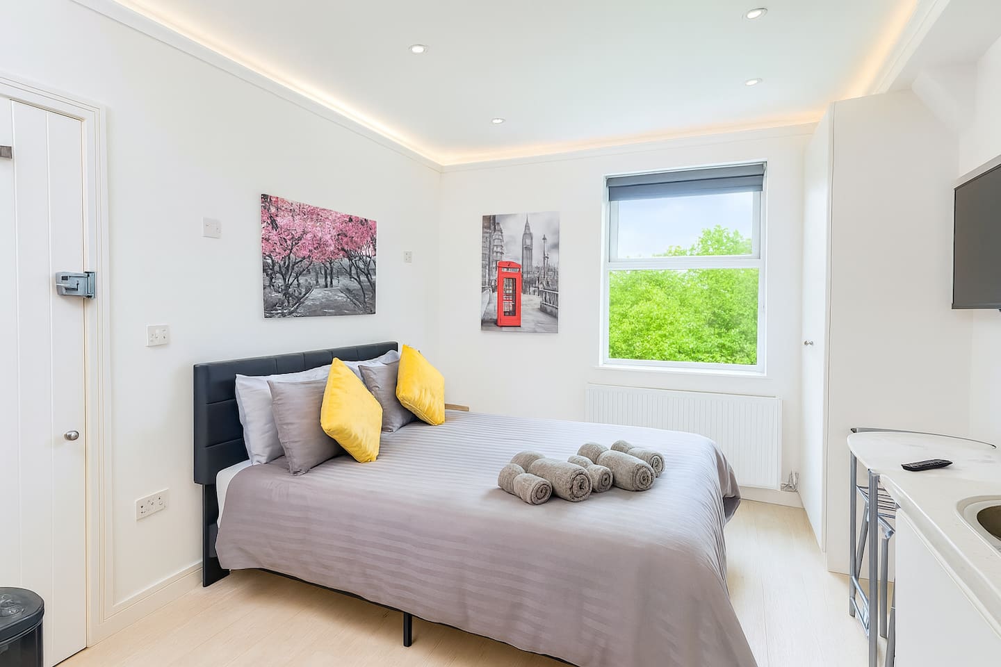 Cozy bedroom with grey bedding, cherry blossom art, and bright natural light.