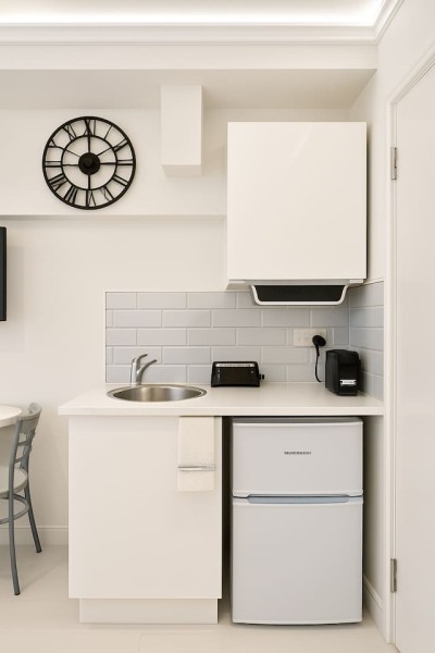 Compact kitchenette with sink, fridge, coffee maker, and modern marble backsplash.