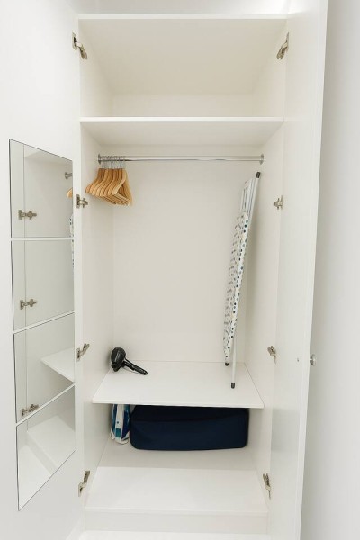 Organized wardrobe with hangers, ironing board, hairdryer, and handy storage shelves.