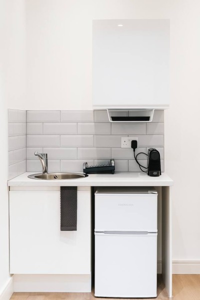 Compact kitchenette with sink, fridge, coffee maker, and sleek modern backsplash.