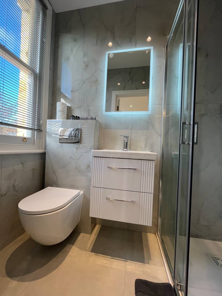Sleek marble bathroom with LED mirror, vanity, and modern glass shower space.