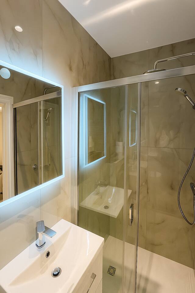 Elegant bathroom with marble tiles, LED mirror, vanity, and sleek glass shower.