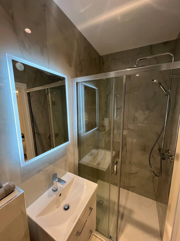 Modern bathroom with marble tiles, LED mirror, vanity, and sleek glass shower.