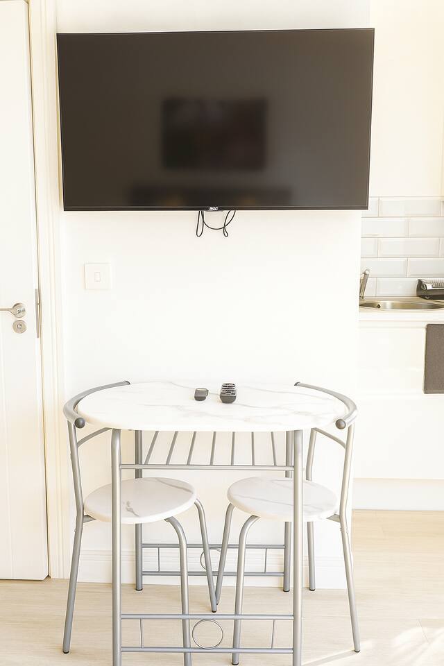 Compact dining nook with marble table, stools, wall-mounted TV, and modern kitchenette.