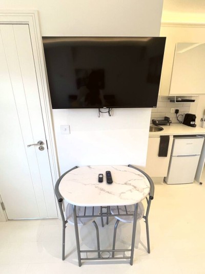 Modern studio with marble table, chairs, wall-mounted TV, and sleek kitchenette.
