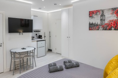 Modern studio with grey bedding, Big Ben art, kitchenette, and cozy dining space.