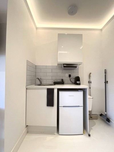 Compact kitchenette with sink, fridge, kettle, and modern grey tile backsplash.
