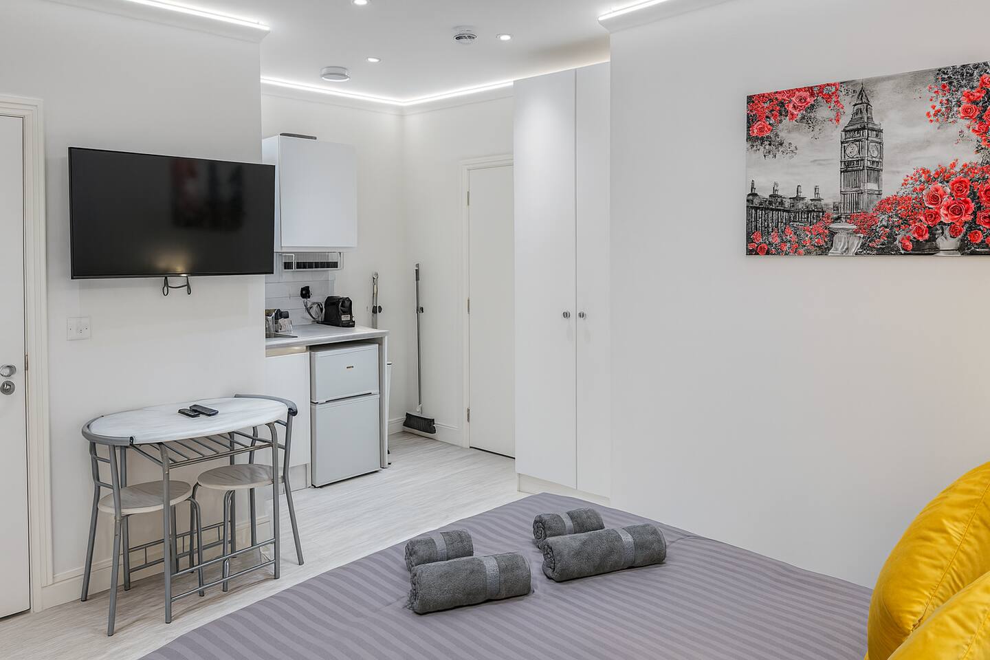 Modern studio with grey bedding, Big Ben art, kitchenette, and cozy dining space.