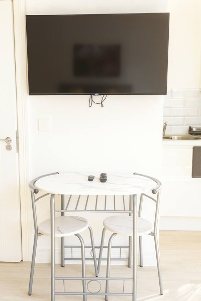Compact dining nook with marble table, stools, wall-mounted TV, and modern kitchenette.