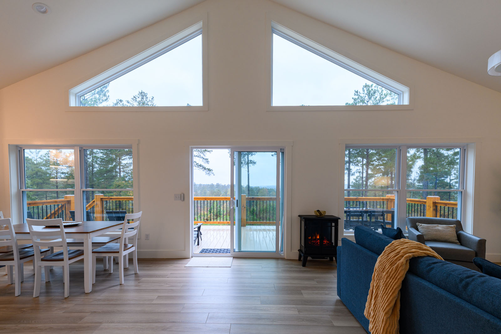 Vaulted great room with panoramic windows, cozy fireplace, and scenic deck views