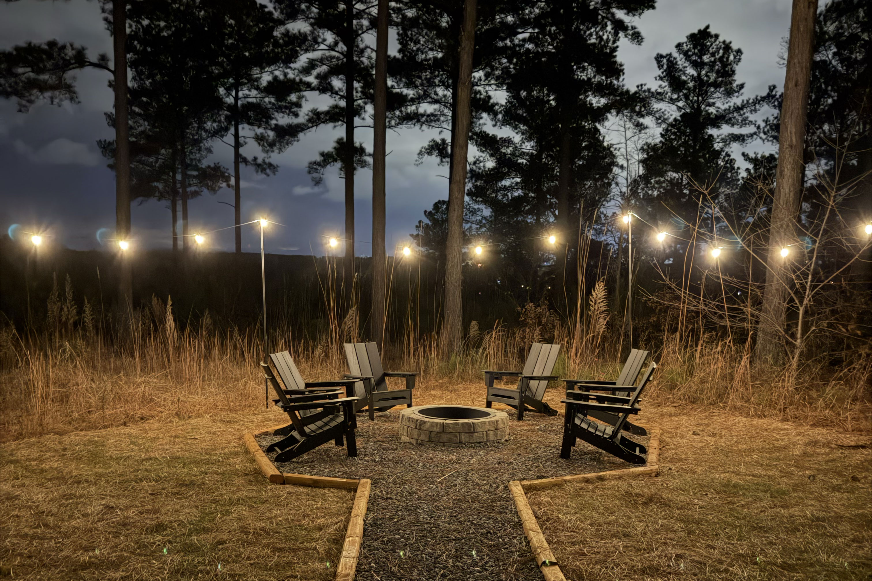 Woodland fire pit lounge with string lights for cozy evenings