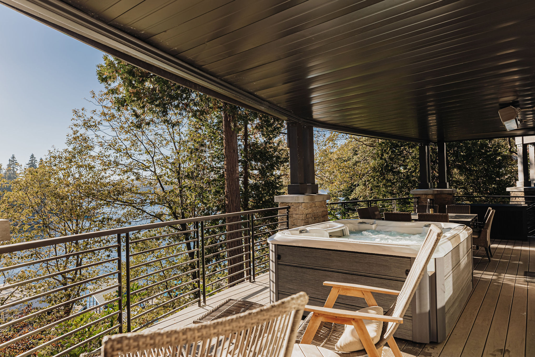 Covered view deck with hot tub, dining area, and peaceful water glimpses
