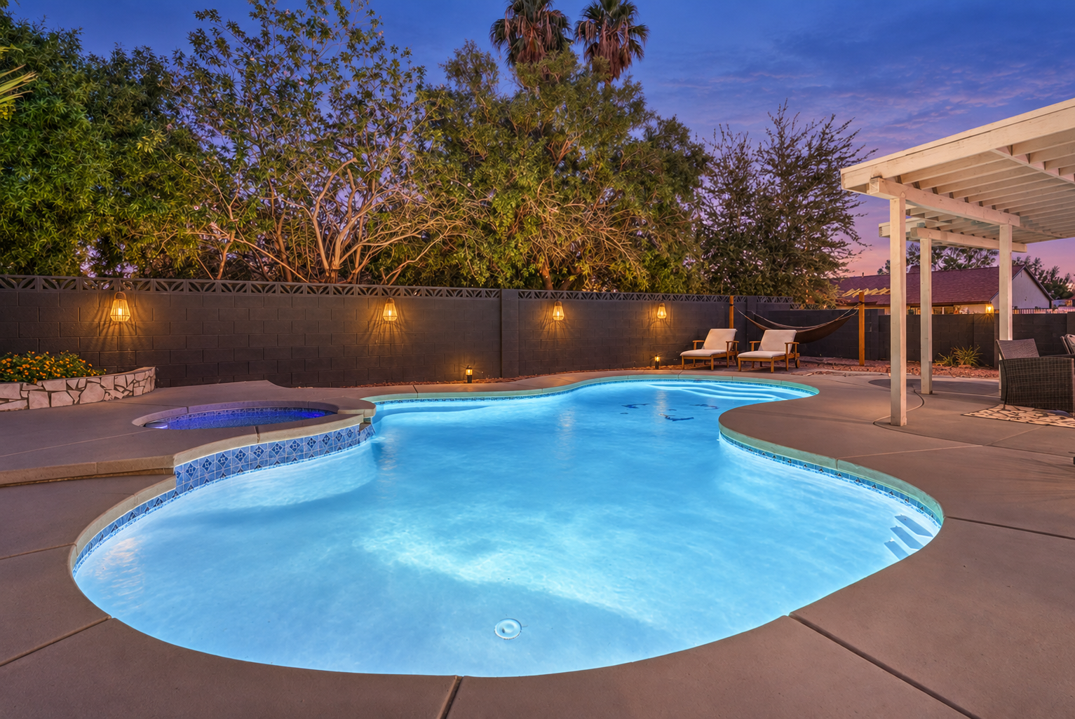 Resort-style backyard with glowing pool, spa, hammock, and sunset ambiance