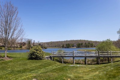 Stroll across the quaint wooden boardwalk as it skirts the lake's edge. Admire the manicured lawn, flowering bushes, and sparkling water with community docks beyond. Perfect for peaceful morning walks or sunset reflections.