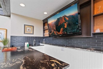 Mix cocktails or watch the big game at this chic bar area with a live-edge countertop, sleek sink and faucet, and massive flat ‑screen TV. Shelves with glassware and a dark tile backsplash create a mountain-modern vibe perfect for happy hour.