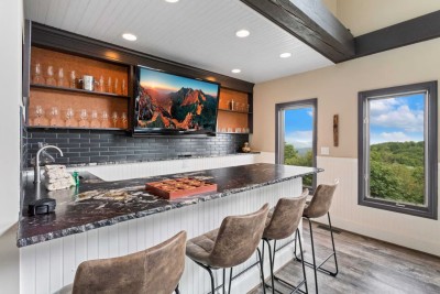 Enjoy breakfast or evening cocktails at this sleek bar with swivel stools, granite countertop, and built-in gas cooktop. Floor-to-ceiling windows frame sweeping mountain views, while rustic beams and open shelving complete the modern mountain vibe.