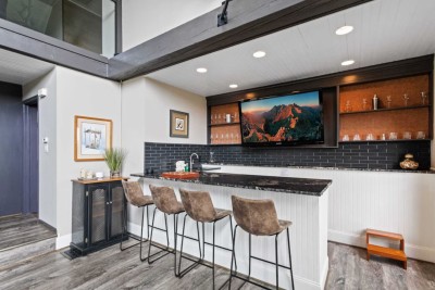 Pull up a stool at this stylish bar with leather seats and watch a movie or chat while dinner simmers. Open beams above, dark tile backsplash and warm wood shelving create a modern yet cozy vibe perfect for happy hour and snacks.