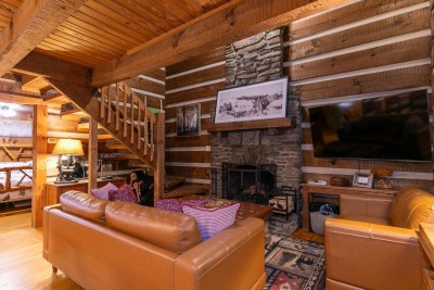 Admire the cabin craftsmanship from this cozy living room with leather sofa, stone fireplace and big-screen TV, and an open staircase leading to the loft.