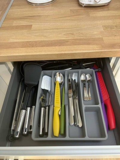 Organized kitchen drawer with colorful utensils and cutlery tray.