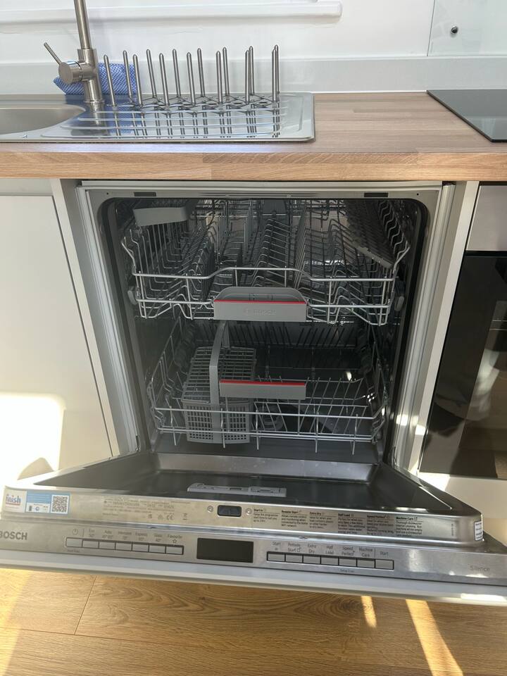 Open Bosch dishwasher in sleek kitchen with wood floors and clean lines.