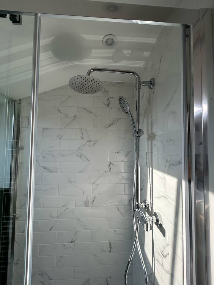 Marble-tiled shower with dual heads and soft natural light.