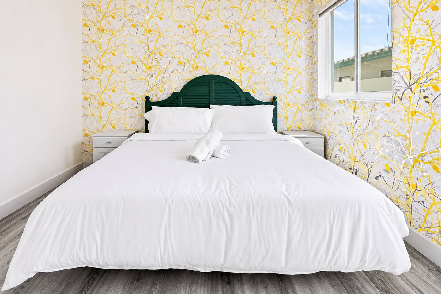 A bright, inviting bedroom featuring elegant botanical wallpaper, a charming arched headboard, and crisp white linens. Natural light fills the space, creating a fresh, peaceful atmosphere perfect for unwinding, recharging, and waking up refreshed.