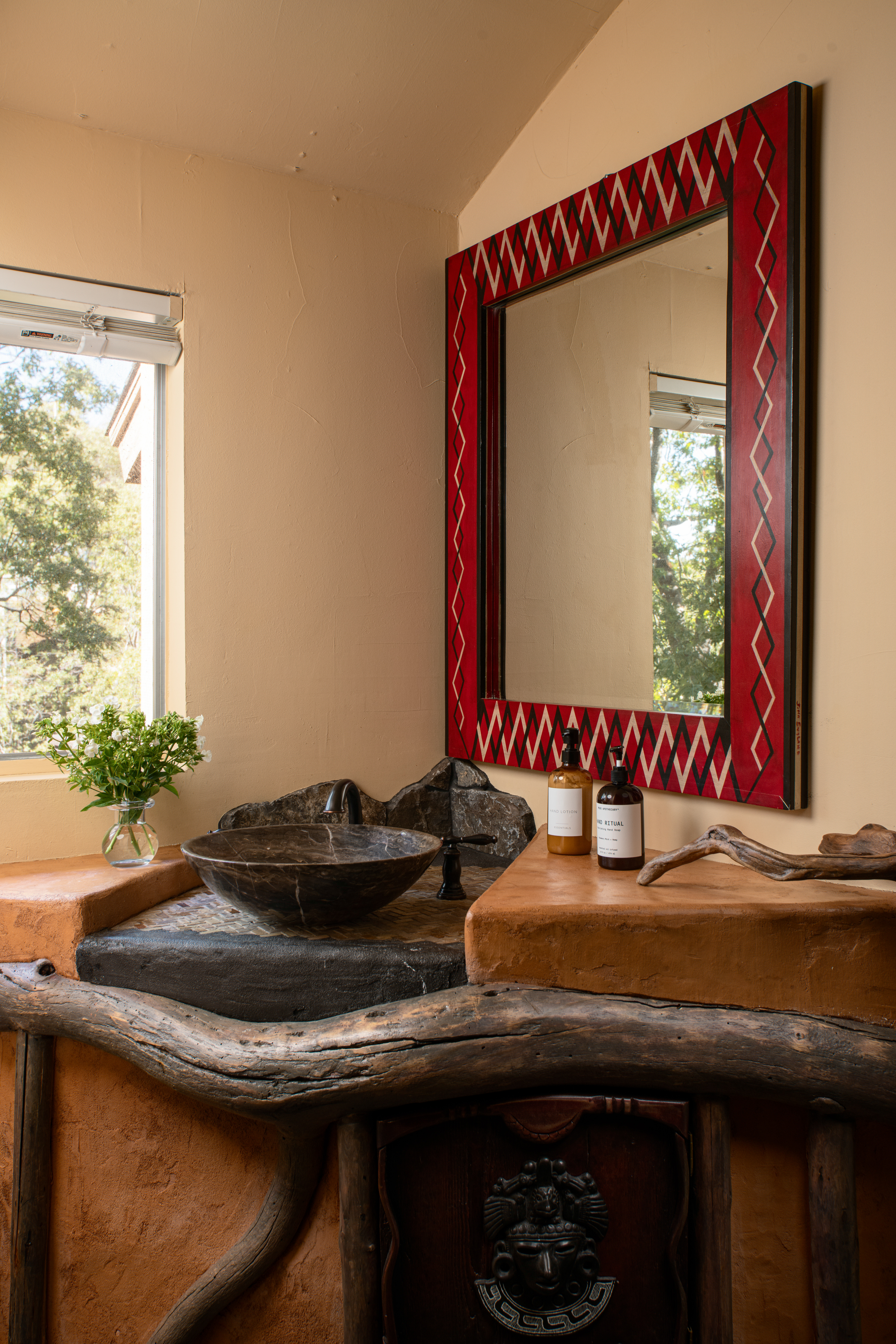 Rustic artisan vanity with stone sink, bold mirror, and natural light