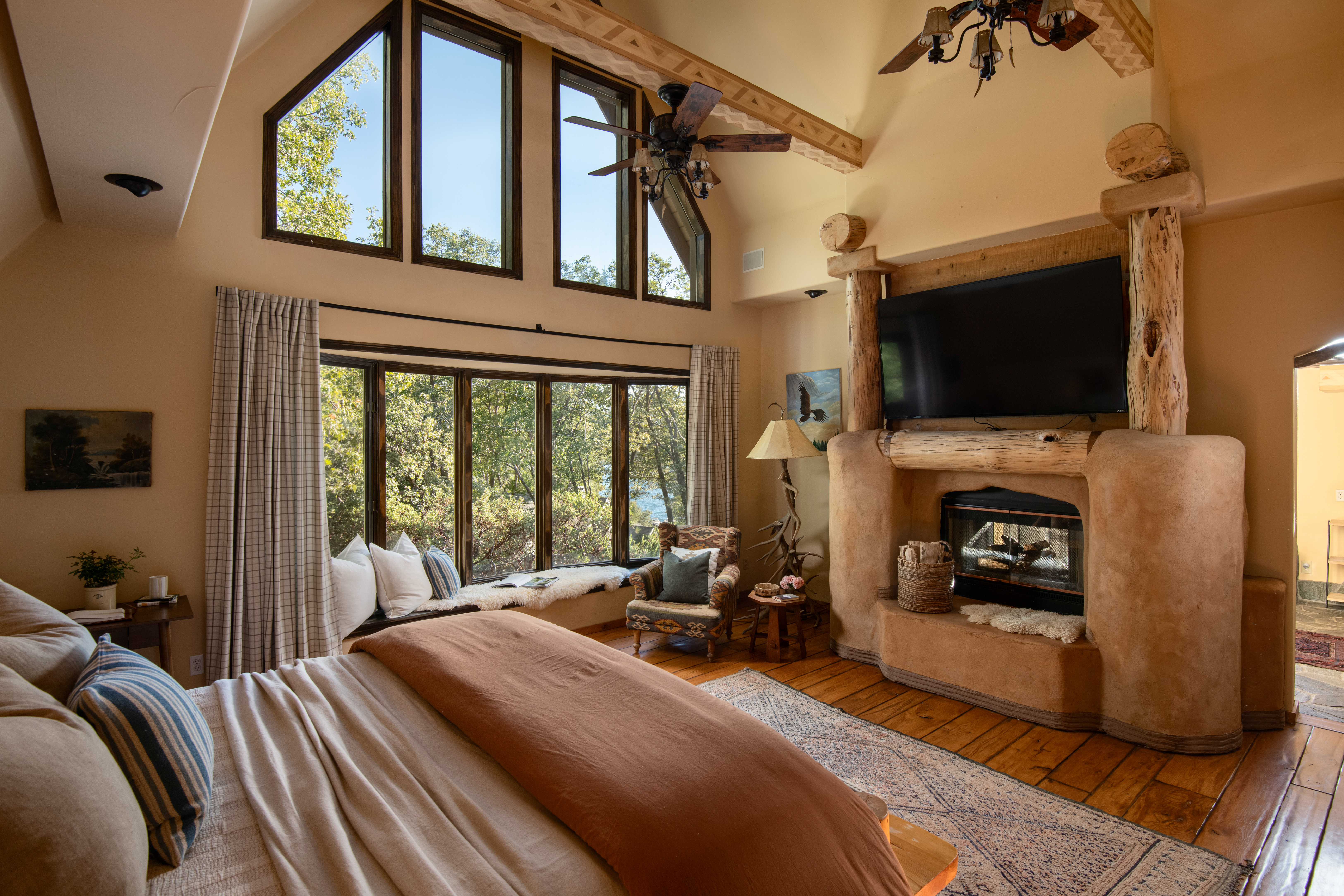 Rustic vaulted bedroom with fireplace, big windows, and serene forest views