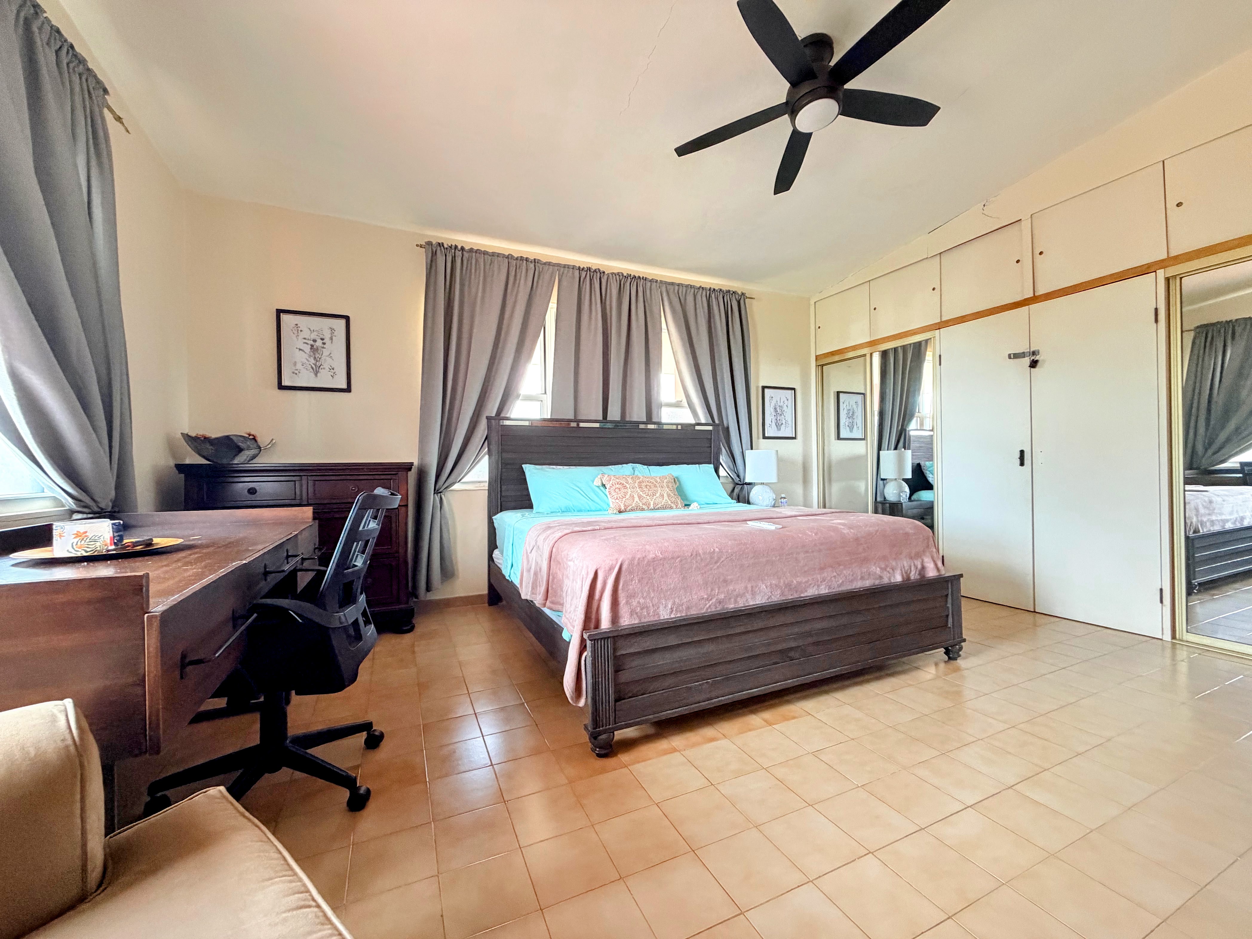 Spacious bedroom with work desk, mirrored closets, and ceiling fan