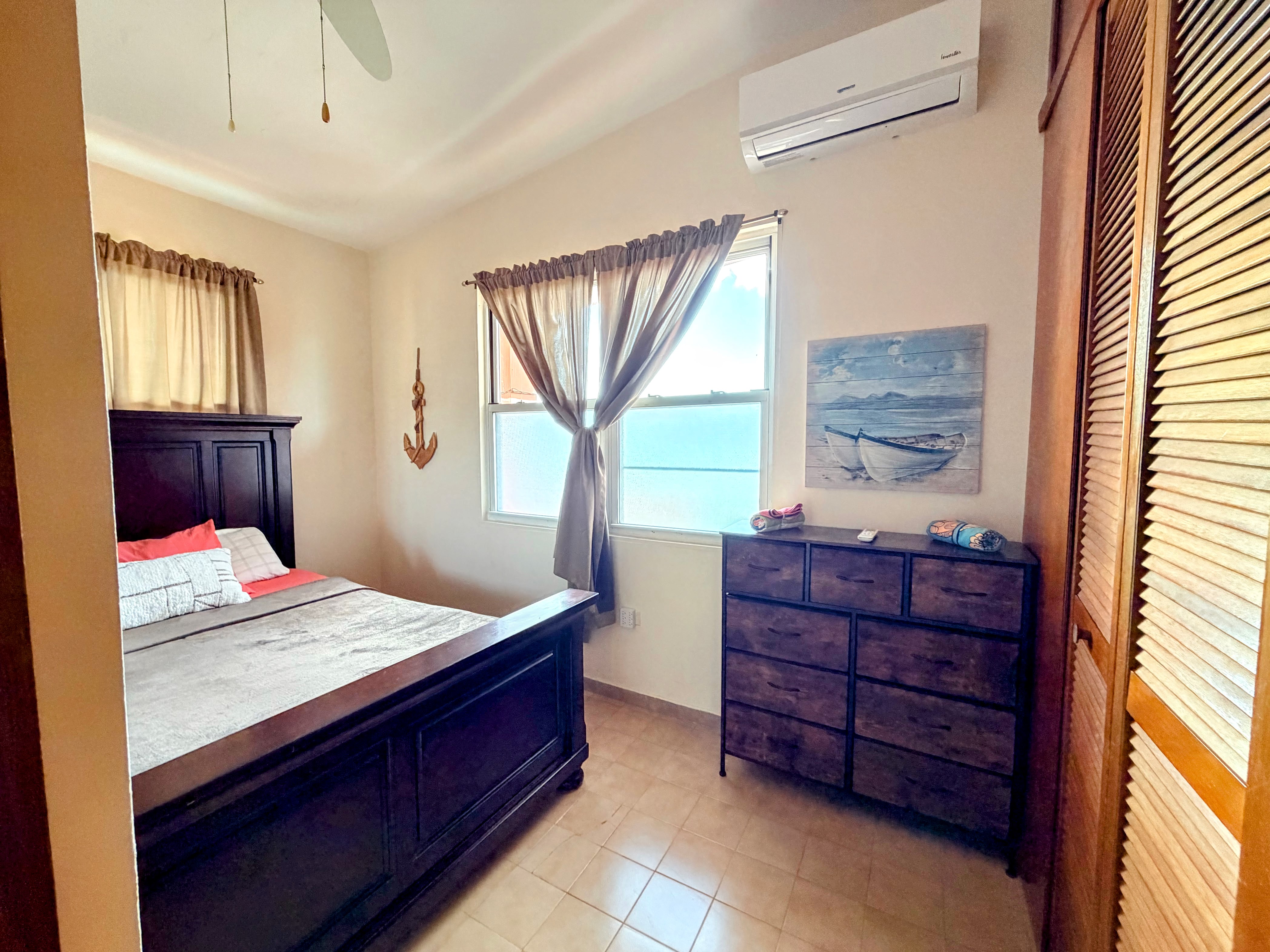 Bright coastal bedroom with AC, natural light, and warm wood furnishings