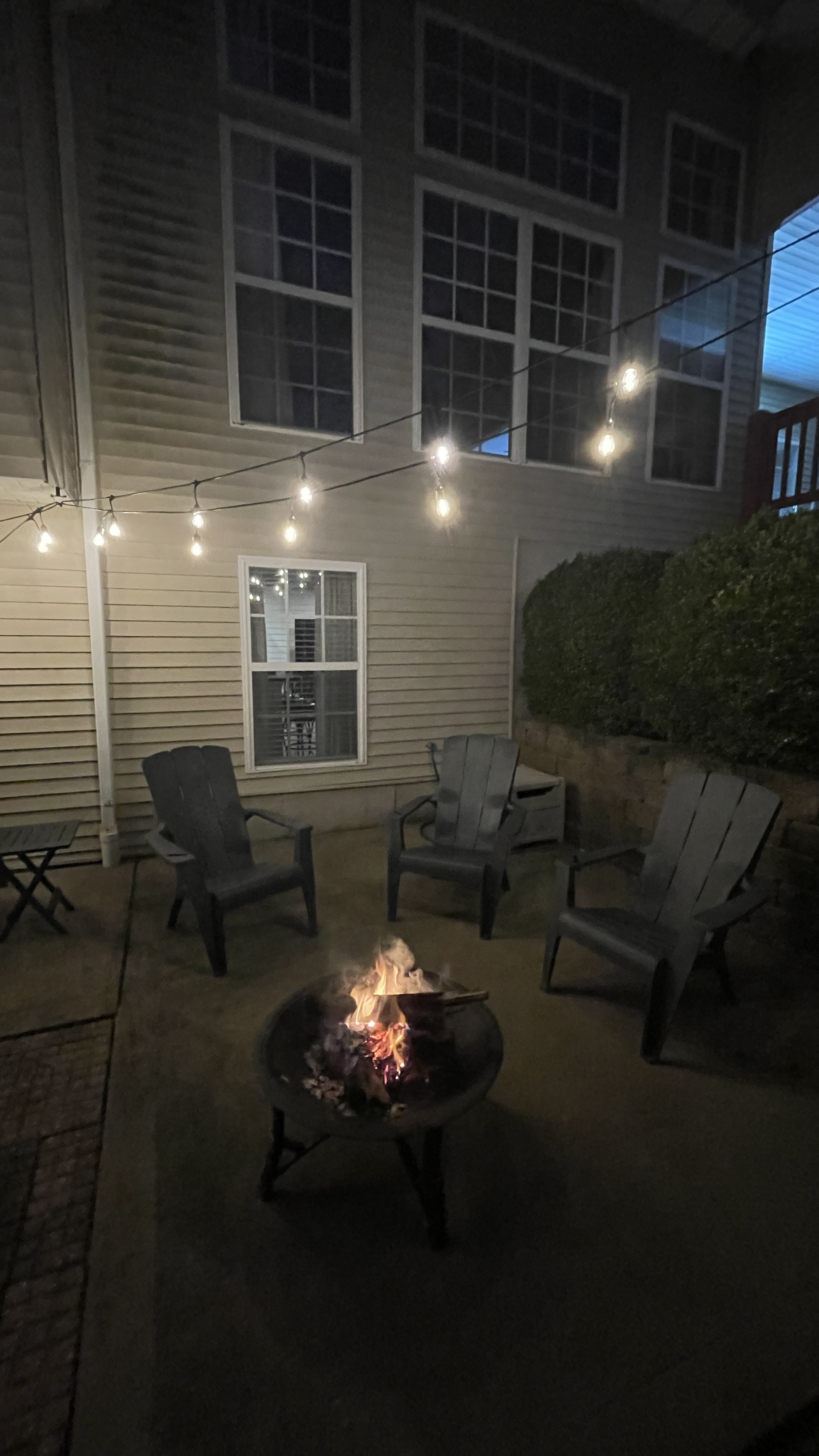 Cozy patio with fire pit, Adirondack chairs, and warm string lights
