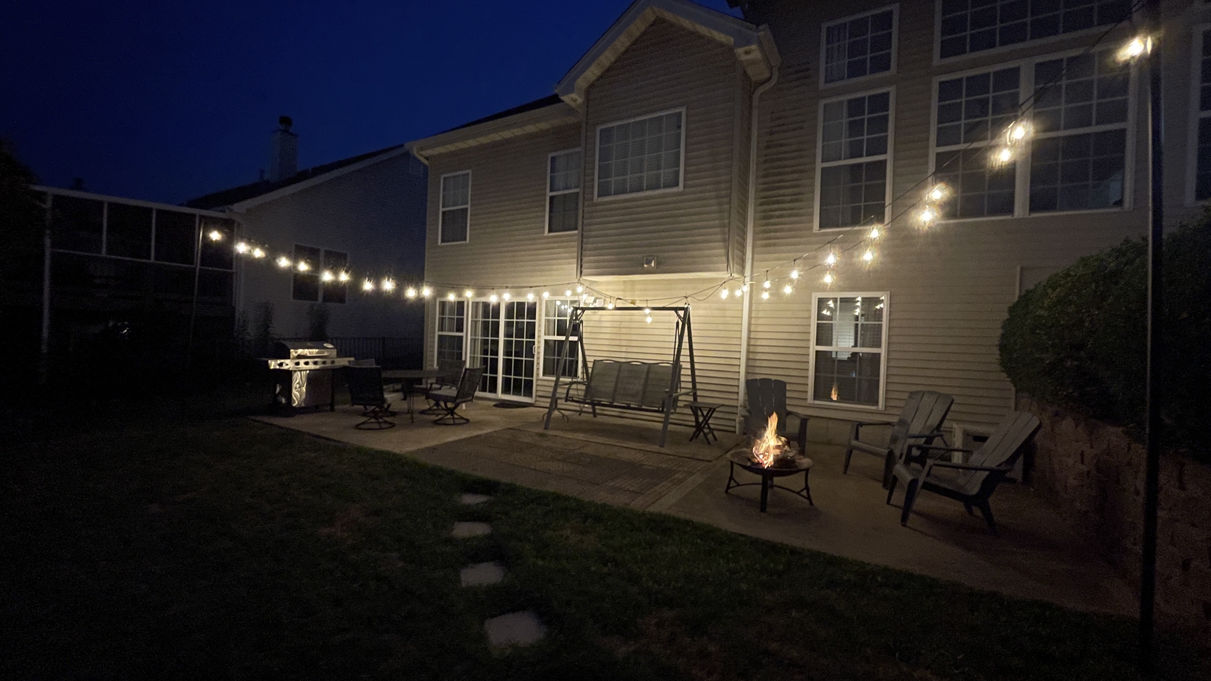 Cozy backyard patio with string lights, fire pit, grill, and swing