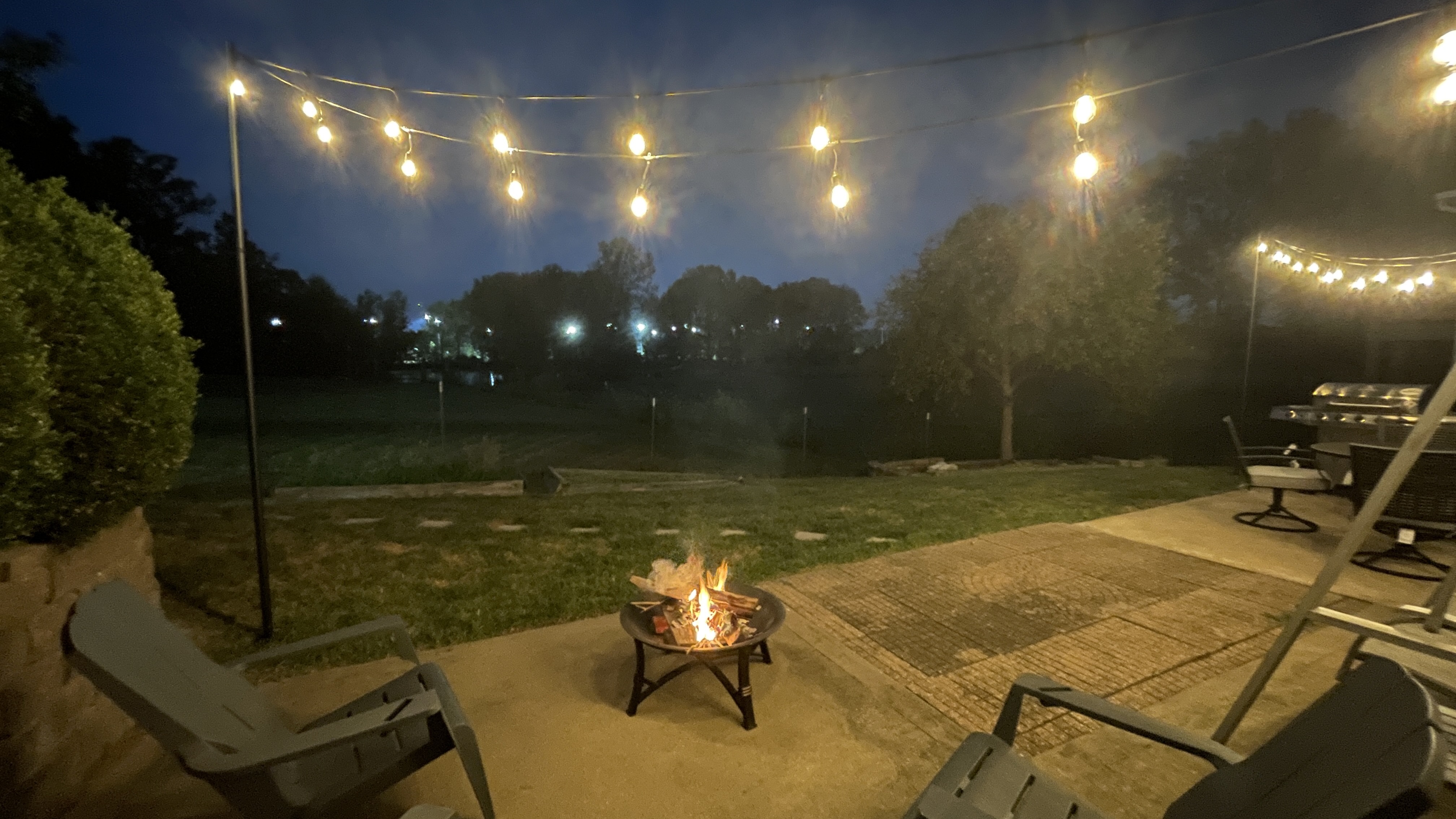 Cozy backyard patio with string lights, fire pit, and open night views