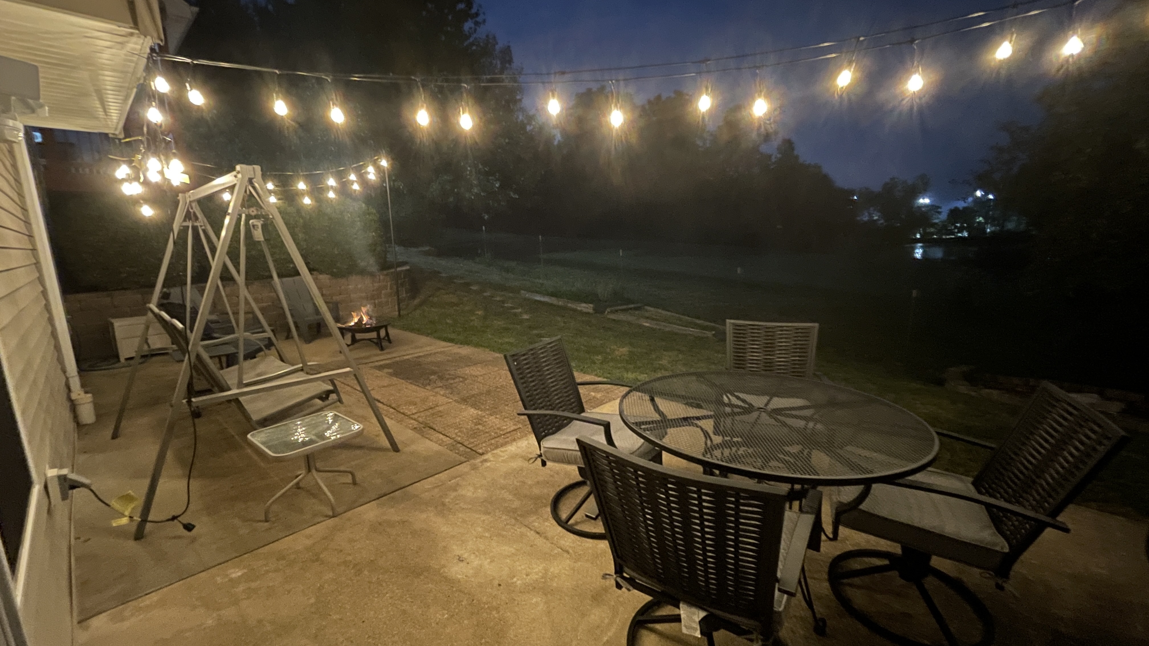 Cozy lit patio with dining, porch swing, and spacious backyard views