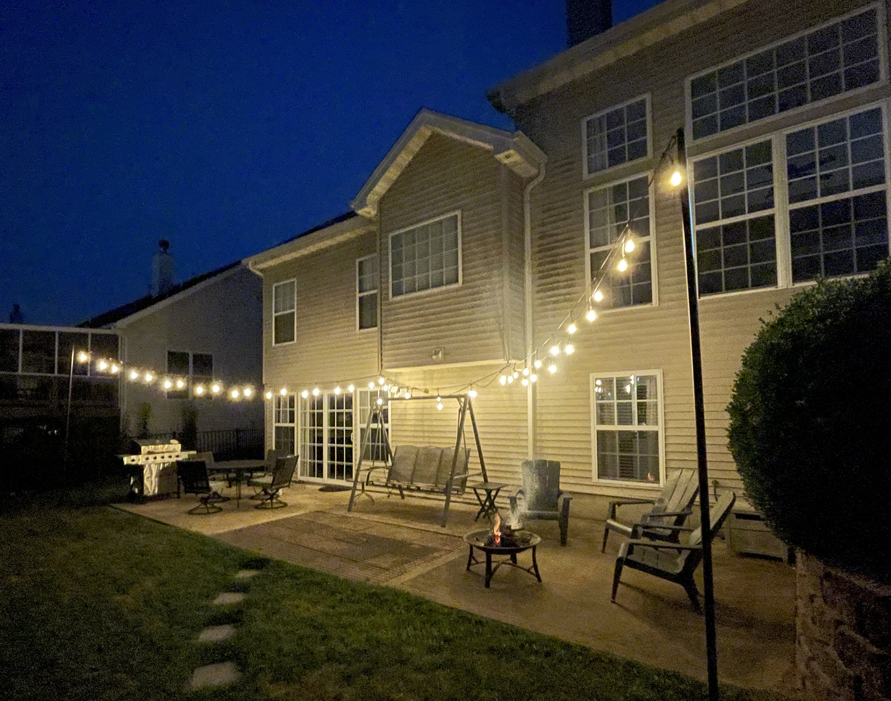 Cozy backyard patio with string lights, fire pit, swing & grill