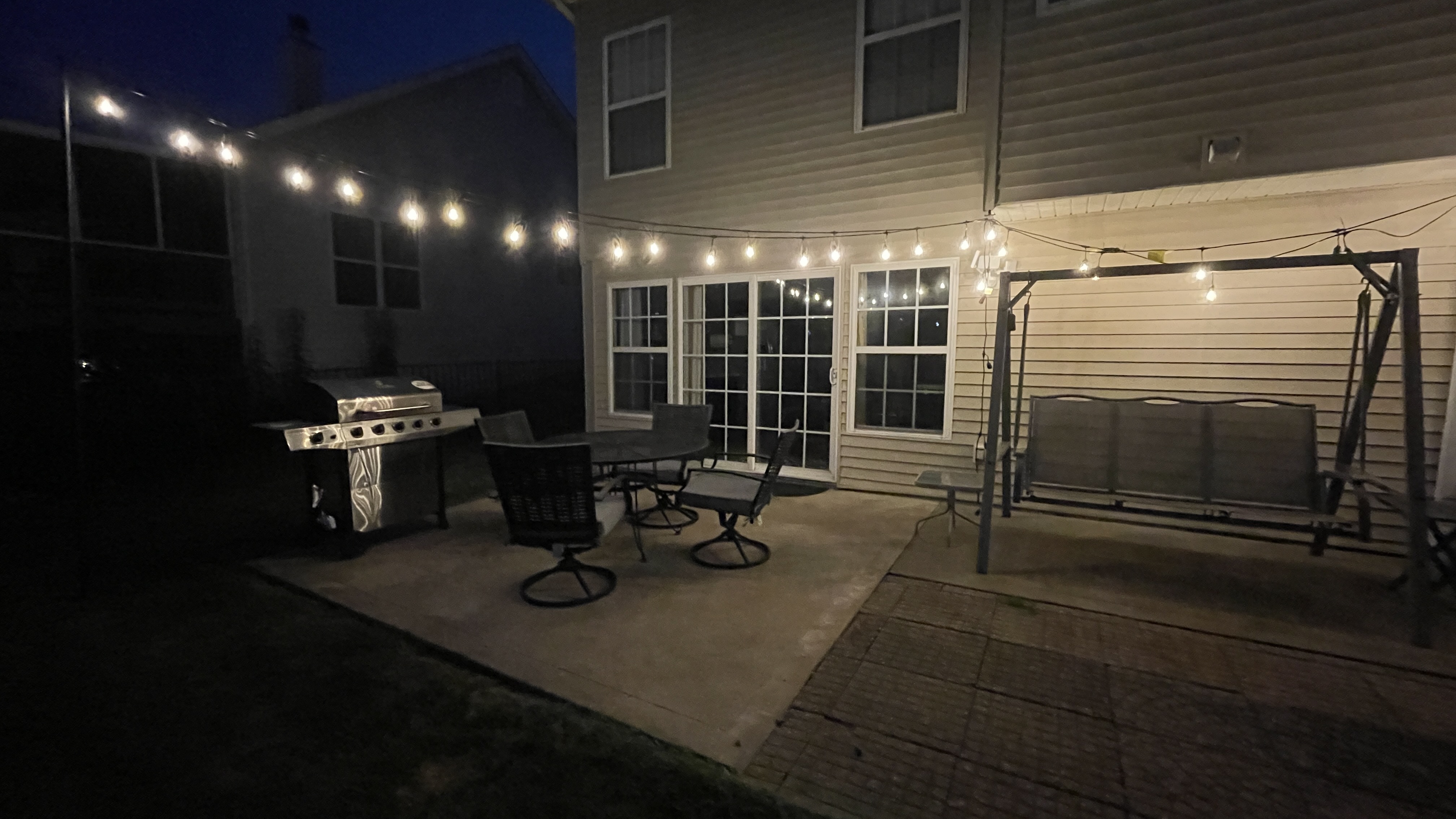 Cozy lit patio with grill, seating, and swing for relaxing nights