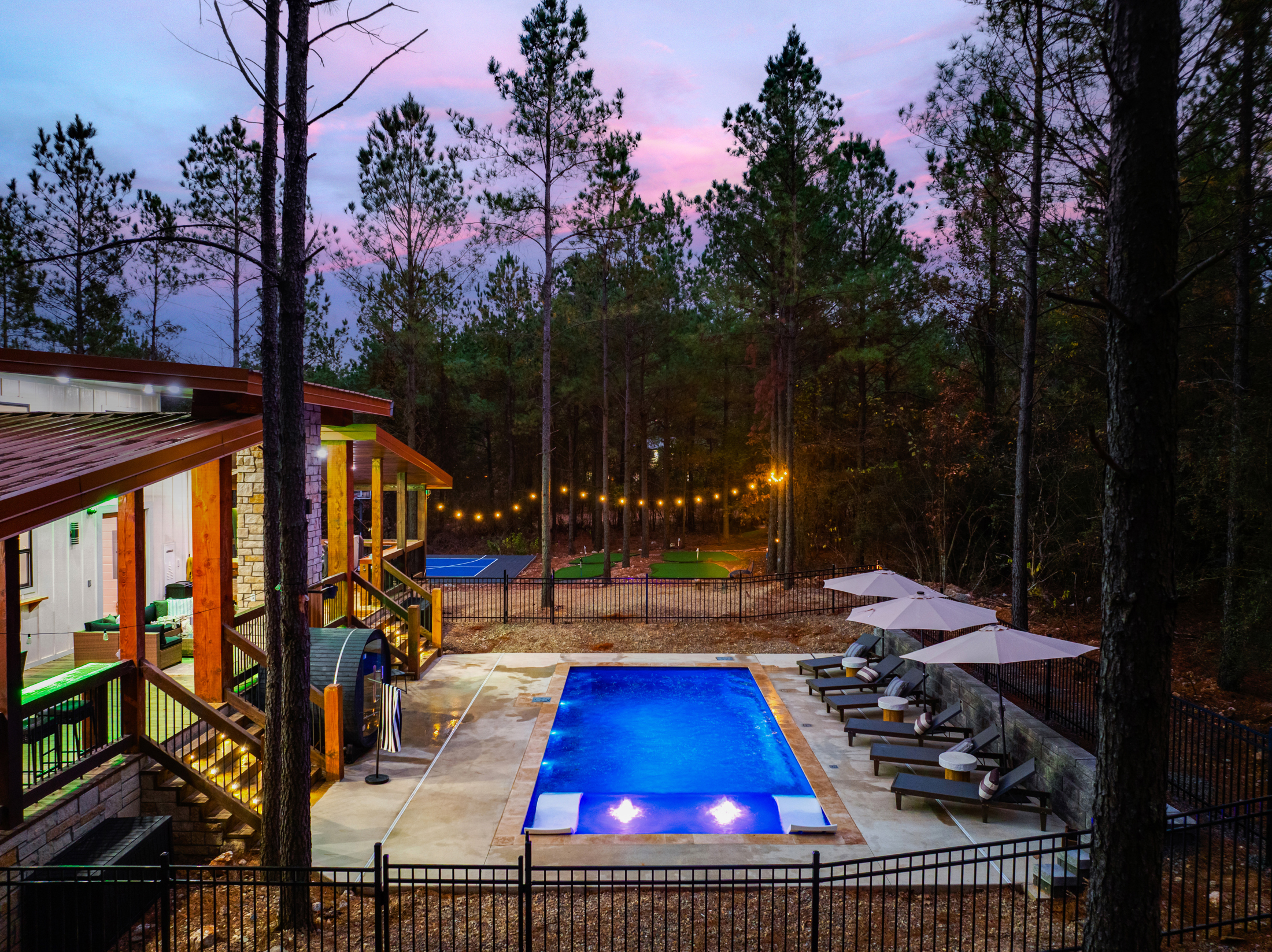 Private wooded pool retreat with lounge seating, string lights, and games