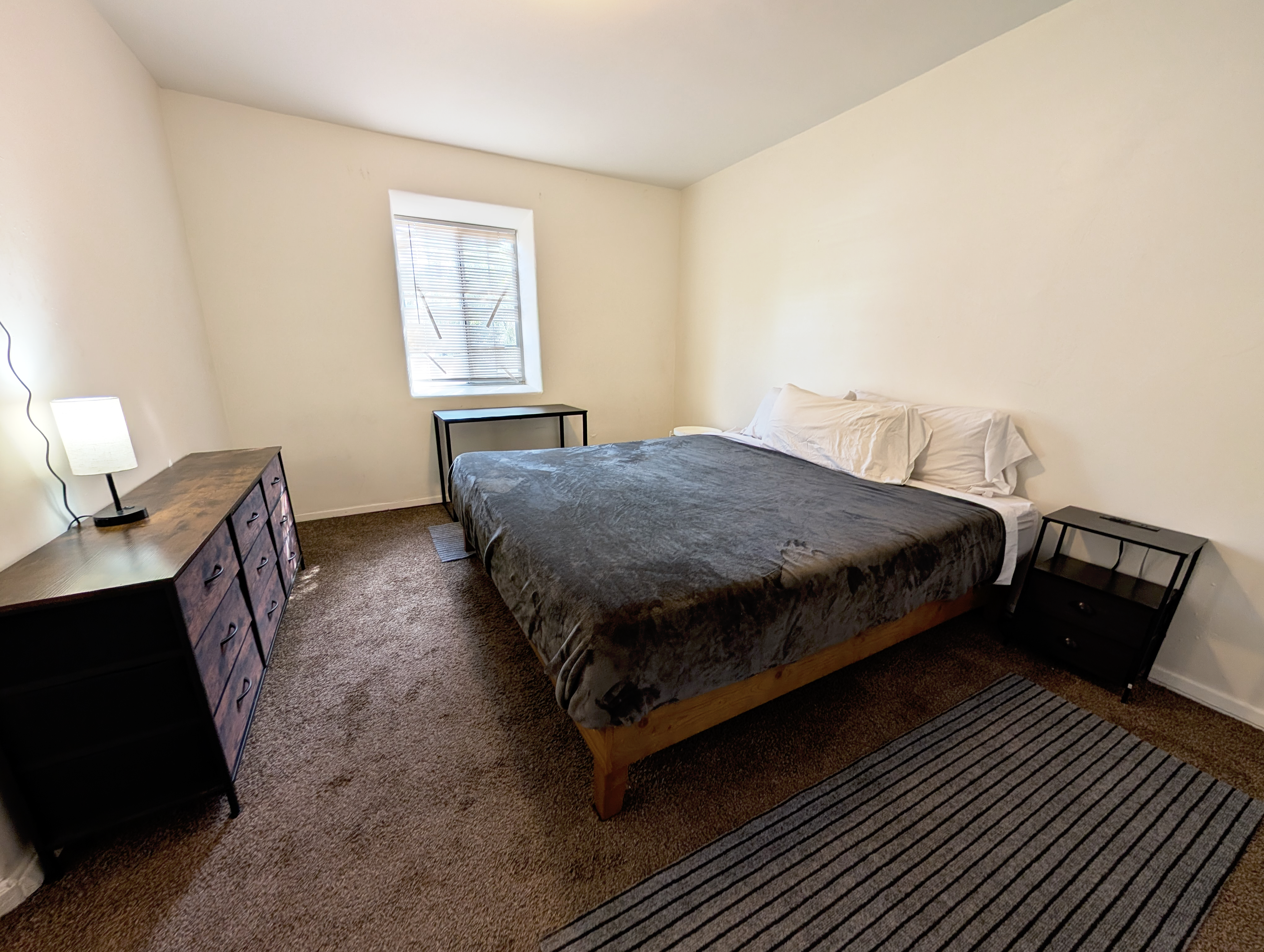 Spacious carpeted bedroom with king bed, natural light, and simple furnishings