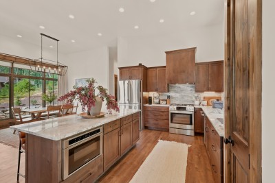 Gather around the oversized quartzite island in this sunlit kitchen, outfitted with a gas range, stainless appliances, and rich wood cabinetry — ready for family meals after a day exploring the High Country.