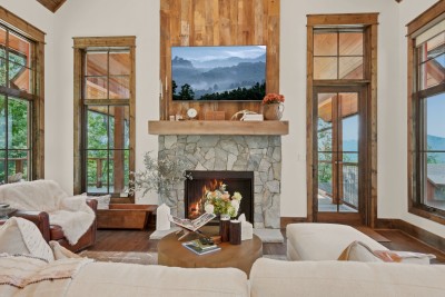 French doors flank the fireplace on both sides, framing layered mountain silhouettes beyond, while a round reclaimed-wood coffee table anchors the seating for game nights or quiet reading.